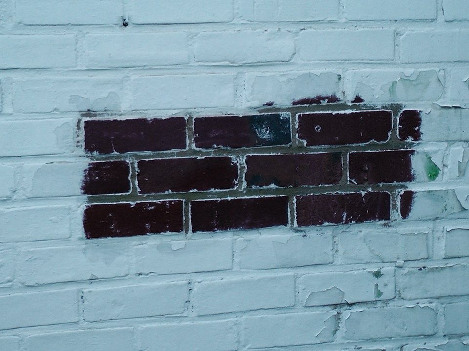 Farbschicht teilweise von einer Backsteinmauer entfernt, roter Backstein sichtbar