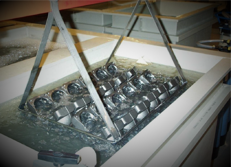 Loading basket with parts above a process tank of a blacking line