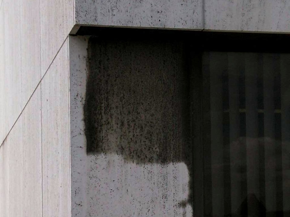 Fassade sandstrahlen: Natursteinfassade neben einem Fenster, teils gereinigt, teils noch schwarz verschmutzt