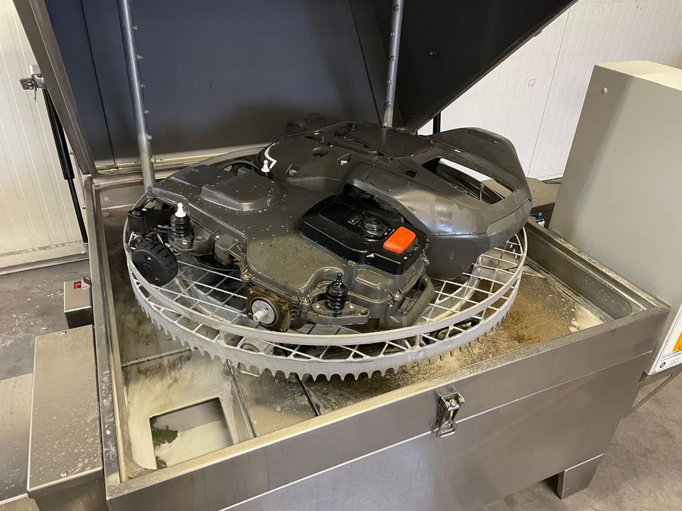 Mähroboter-Winterservice: Chassis auf dem Drehkorb eines geöffneten Teilewaschautomaten, über dem Bad
