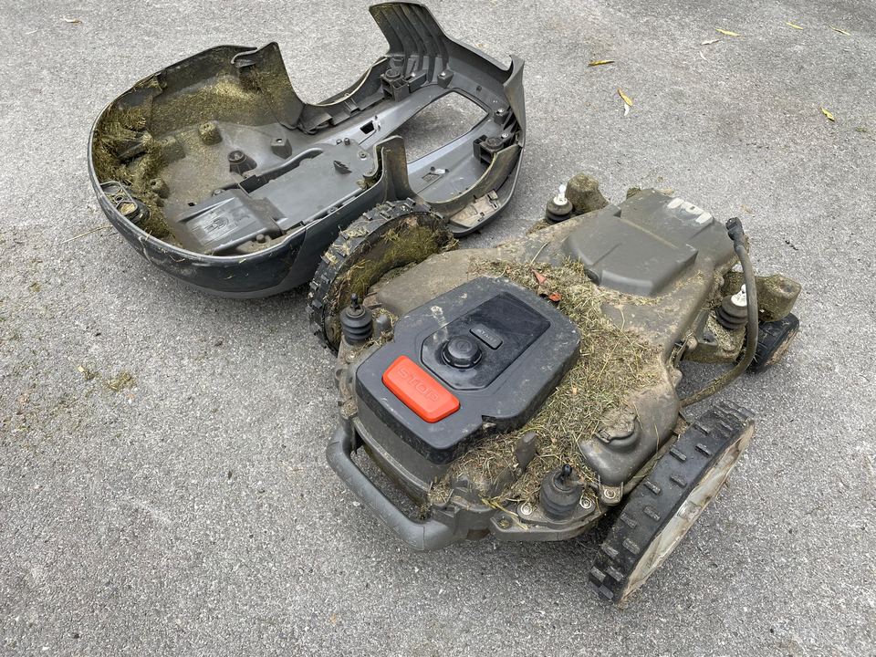 Mähroboter mit abgenommener Haube, das Chassis voller Schmutz