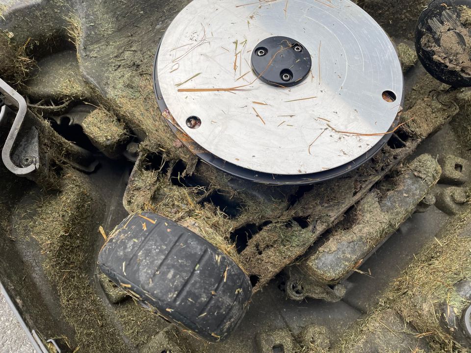 Mähscheibe und Rad eines Mähroboters mit festgebackenem Gras