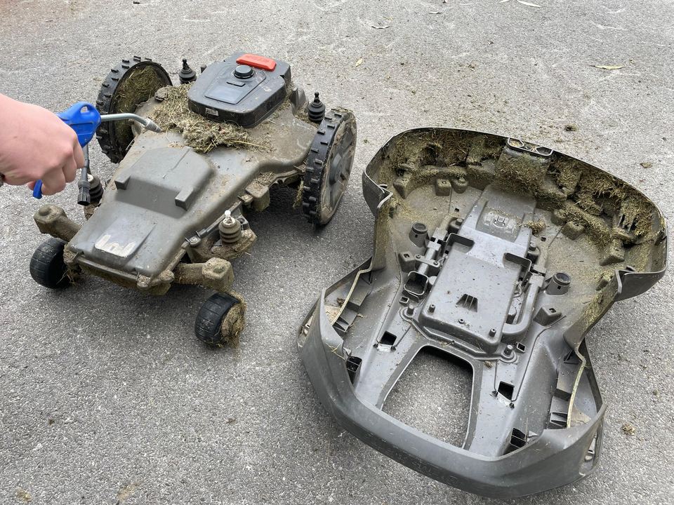Mitarbeiter bläst das Chassis eines Mähroboters mit Druckluft ab