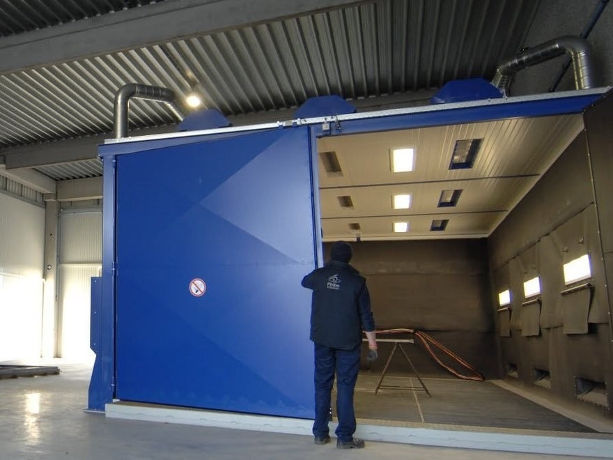 Blue blast room with its door open onto the lit blasting area, in a workshop
