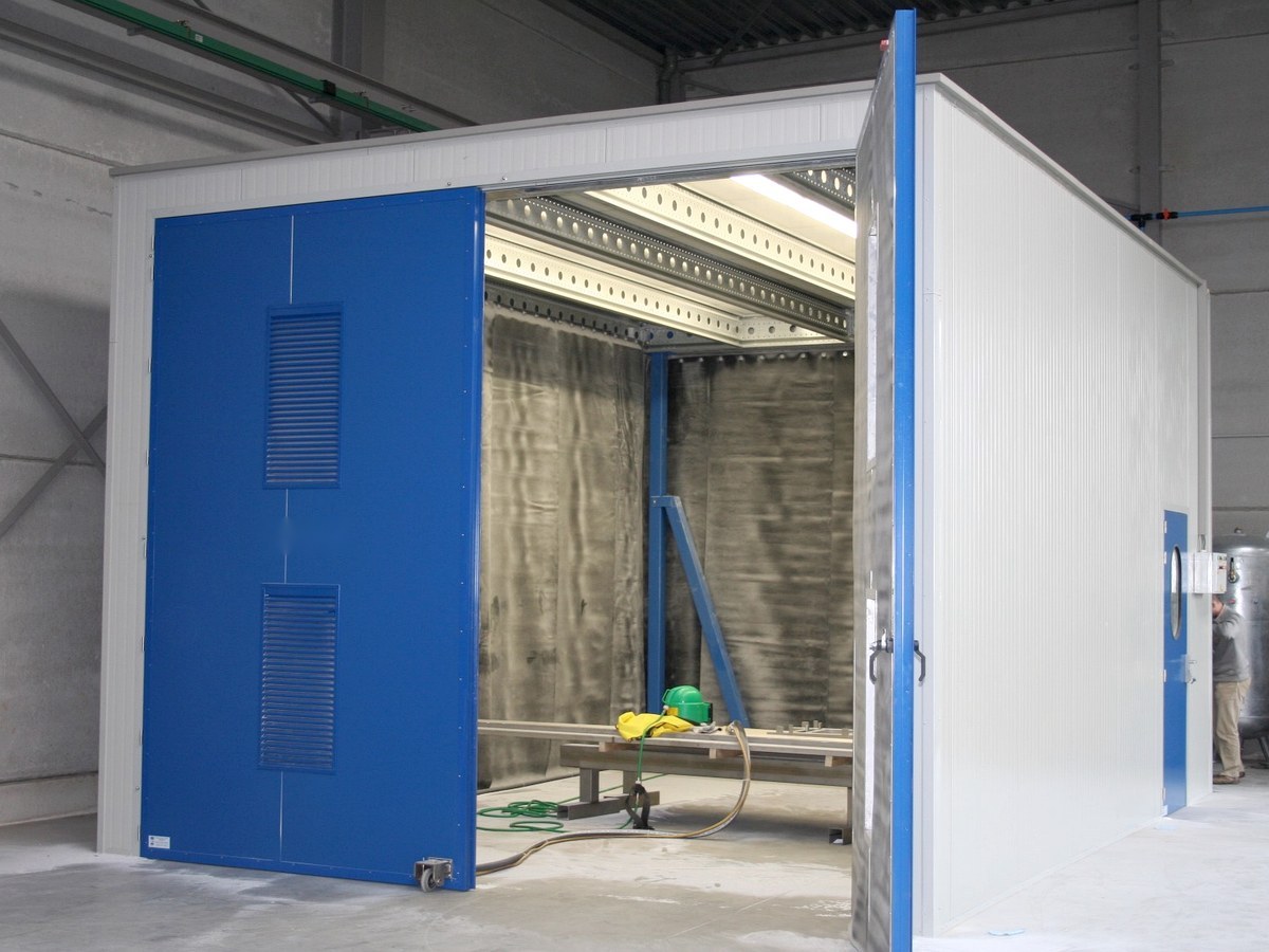 Free-standing walk-in blast cabin with blue doors, installed in an existing workshop