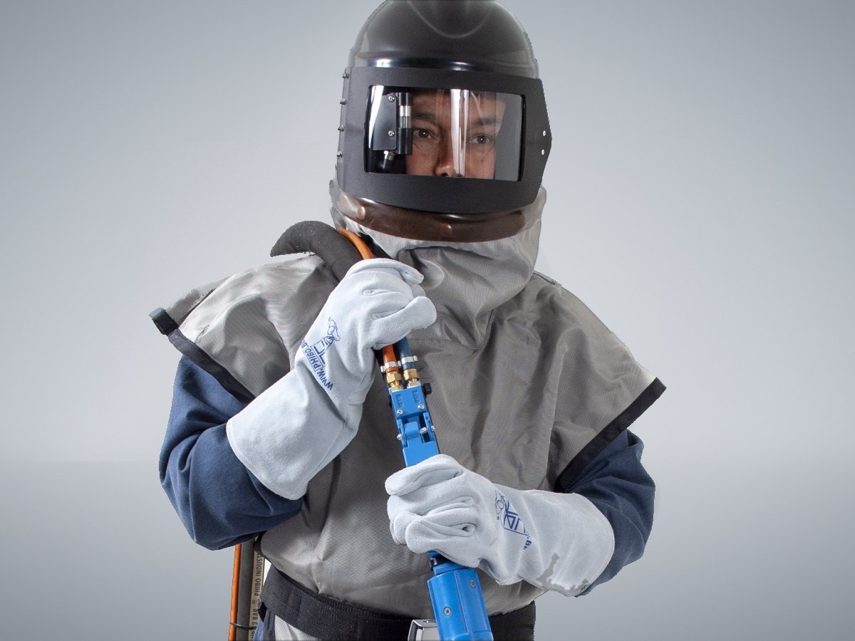 Operator wearing a blast helmet with the cape over the shoulders, blast hose with deadman handle in hand
