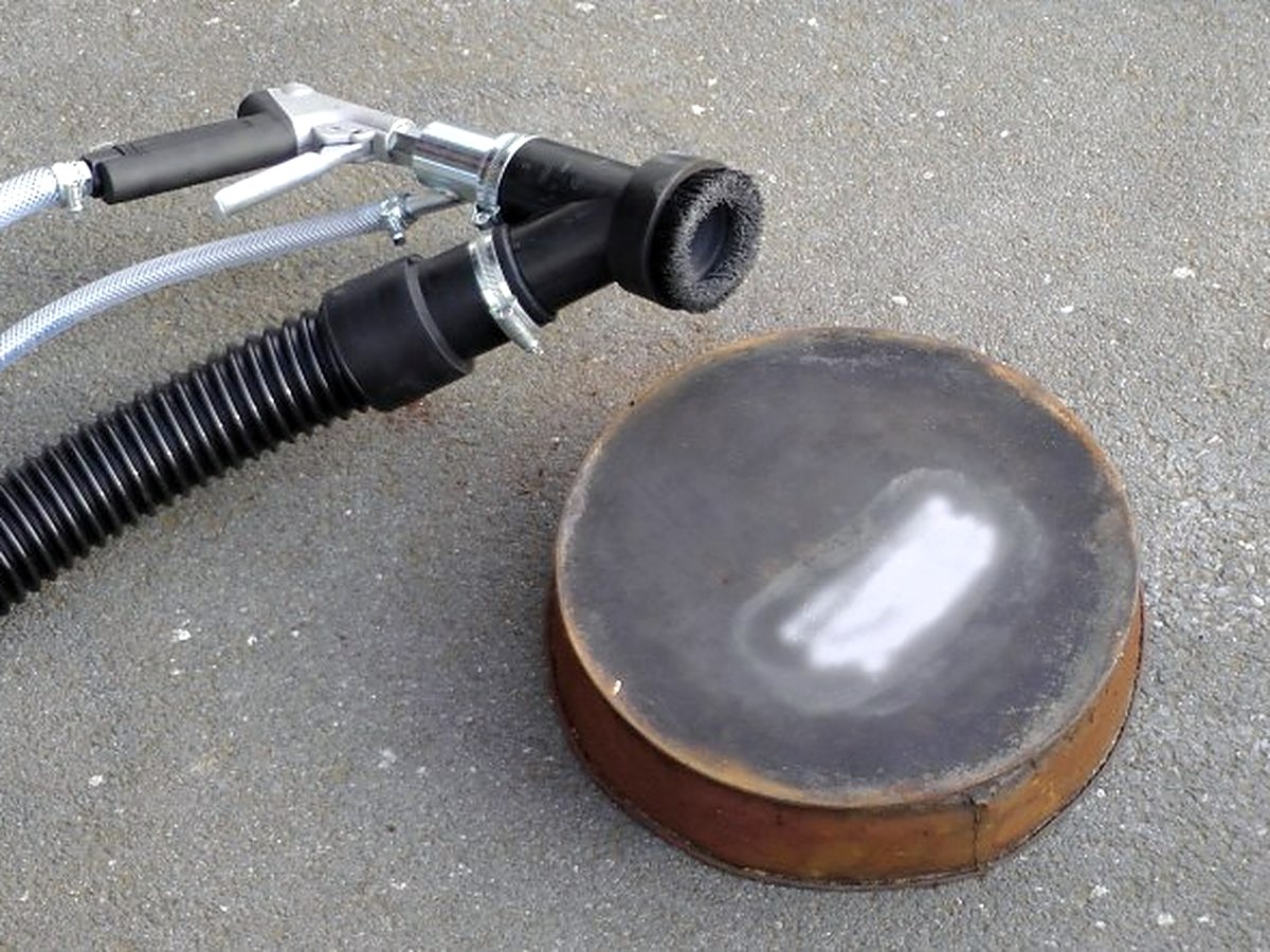 Koperen schijf op de grond, met in het midden een ovale plek die blank gestraald is